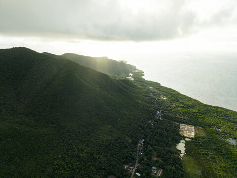 Aerial view of lush, green forest meeting the bright, shimmering ocean under a cloudy sky, Karimunjawa, Central Java, Indonesia.