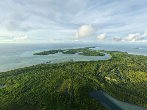 Aerial view of a lush green island meeting turquoise waters under a soft, cloud-dappled sky, Karimunjawa, Central Java, Indonesia.