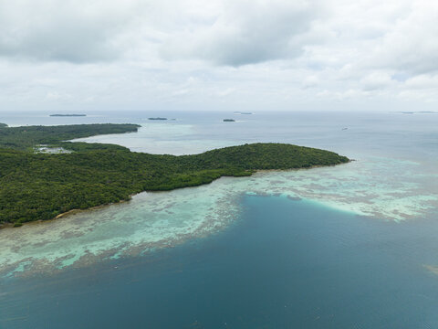 Aerial view of the vibrant turquoise waters meeting the lush green coastline under a cloudy sky, Karimunjawa, Central Java, Indonesia.