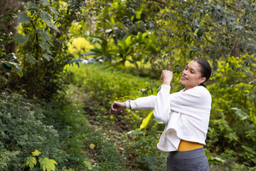 Woman stretching right arm across chest on wooded trail in fleece and smartwatch, copy space © wavebreak3