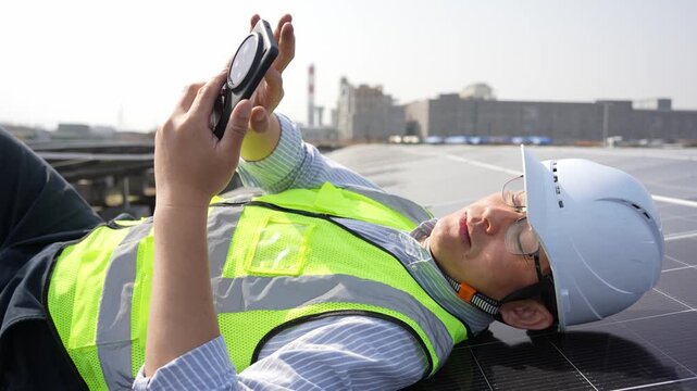 Engineer lying on rooftop checking photovoltaic panel data with handheld device