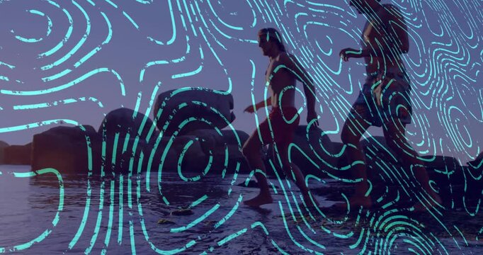 Pair walking rocky shore for travel, woman stepping into surf and creating cyan overlay splashes