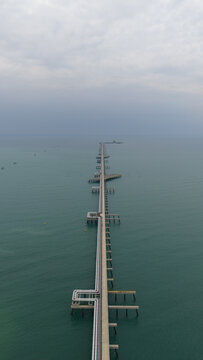 Aerial view of a long pier stretching into the sea under a cloudy sky, Map Ta Phut, Rayong, Thailand.