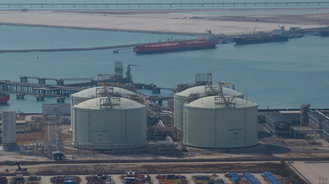 Aerial view of massive white industrial tanks gleaming under the sun next to a harbor with ships, Map Ta Phut, Rayong, Thailand.