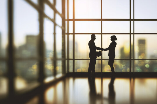 Business partners or employees shaking hands in a modern office with glass windows, soft blurred focus, symbolizing technology and management