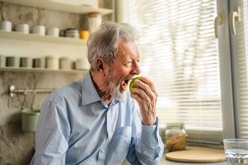 Fototapeta premium Senior adult man holding green apple in kitchen