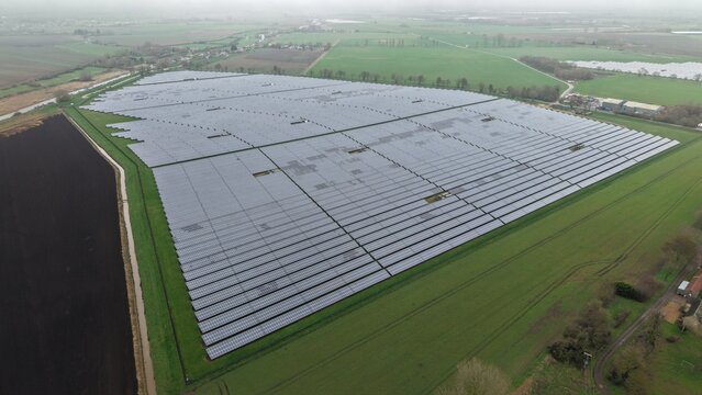 Aerial view of a vast solar farm glinting under the diffused light, a modern landscape of clean energy nestled within the green fields, Cambridge, England, United Kingdom.