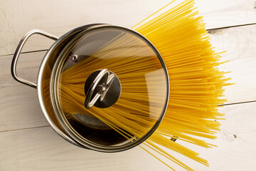 Fototapeta premium Uncooked spaghetti with kitchen utensils on wooden table, close-up. Top view.