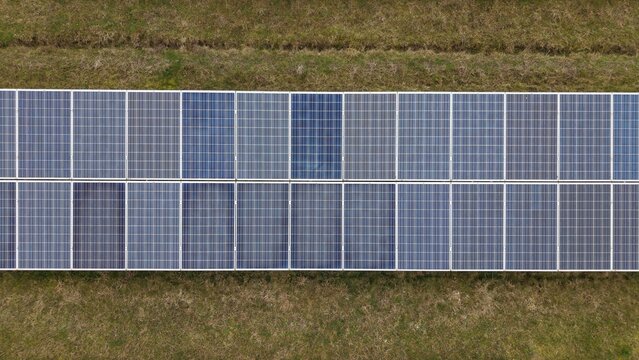 Aerial view of solar panels gleaming softly amidst bordering green fields, a symphony of modern technology harmonizing with nature's tranquility, Huntingdon, Cambridgeshire, United Kingdom.
