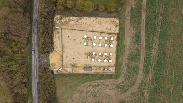 Aerial view of a grid of white domes standing starkly against the sandy ground, surrounded by fields and a road, Alconbury, Huntingdon, United Kingdom.