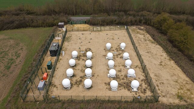 Aerial view of a cluster of pristine white domes standing in stark contrast against the muted, earthy tones of the surrounding landscape, Alconbury, Huntingdon, United Kingdom.