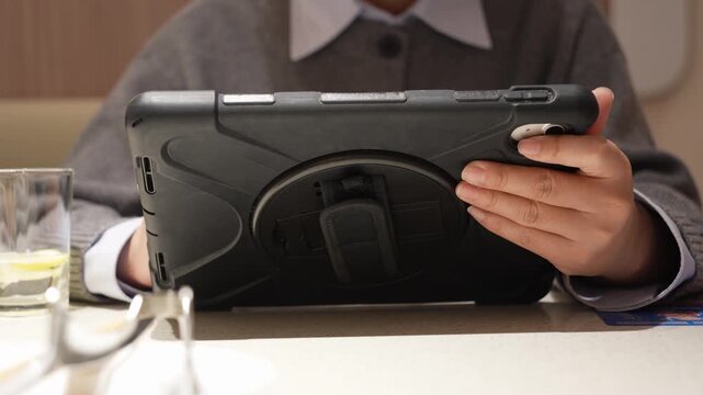 Student in school uniform holding a tablet computer while dining at a table
