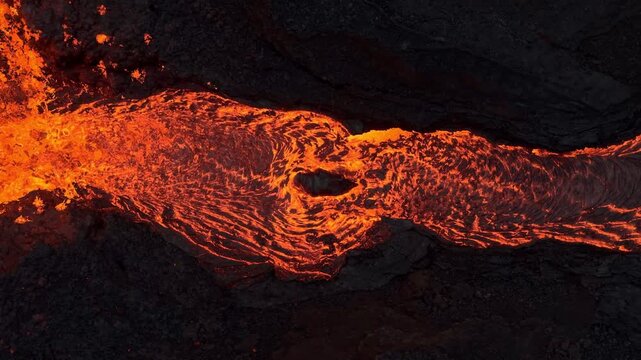 Aerial view of a river of bright orange lava flowing through dark, volcanic rock, creating a stark contrast, Grindavik, Grindavikurbaer, Iceland.