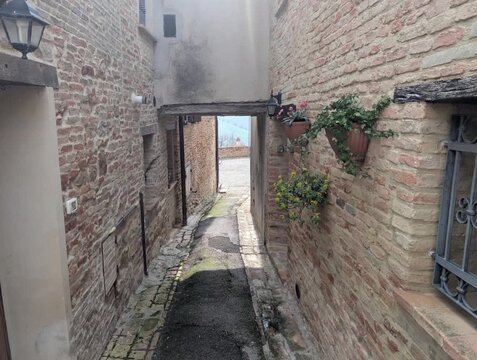 Vicolo tra edifici in mattoni, con pavimentazione mista in pietra e asfalto che conduce verso una zona luminosa sullo sfondo