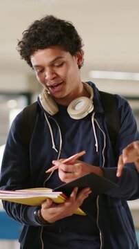 Vertical video: Watching peer gesturing student taking notes in hall with yellow notebook metal pen