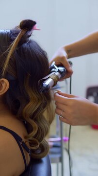 Hairdresser curling woman's long hair in beauty salon with iron styler