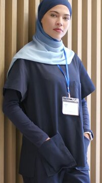 Vertical video: Camera cueing clinician adjusting pose in clinic, showing navy scrubs, hijab, badge