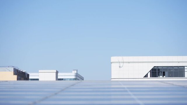 Worker carrying a solar panel while inspecting rooftop photovoltaic arrays under clear blue sky