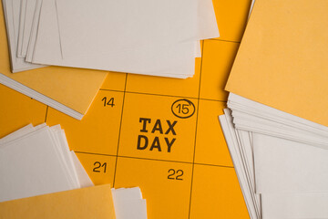 Obraz premium Tax Day. Yellow Wall Calendar Marked Tax Day April 15 and Surrounded by Stacks of Paperwork. Top View