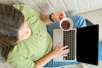 Woman typing on a laptop and holding a cup of tea, working remotely