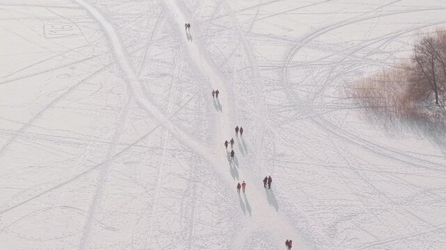 Aerial view of people walking on the frozen Lake Galve, their shadows stretching across the vast expanse of icy white, Trakai, Lithuania.