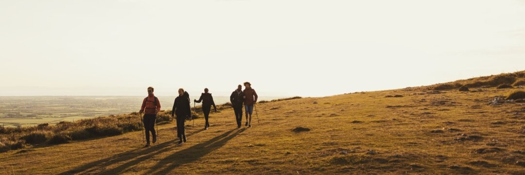 Group of people walking on a grassy hill at sunset. Silhouettes of friends enjoying nature. Outdoor adventure on a hill. Peaceful sunset walk on a hill. Hiking on nature trail.