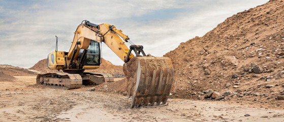 Heavy machinery moves soil and rocks at a construction site. The excavator digs into the ground while piles of dirt surround the area during the day © Anoo
