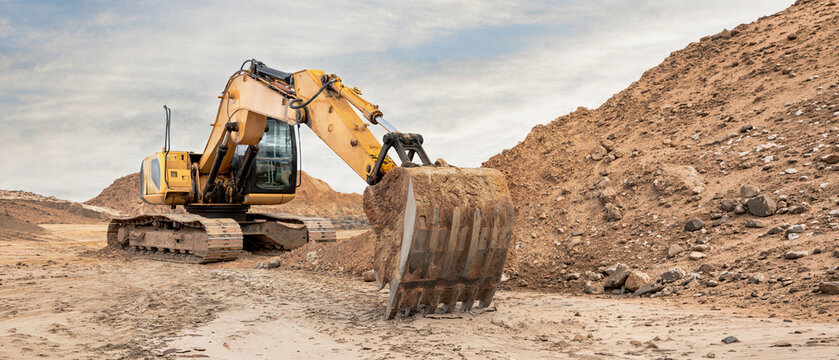 Heavy machinery moves soil and rocks at a construction site. The excavator digs into the ground while piles of dirt surround the area during the day