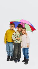 Three boys standing under colorful umbrella wearing mid season kids fashion outfits in studio....