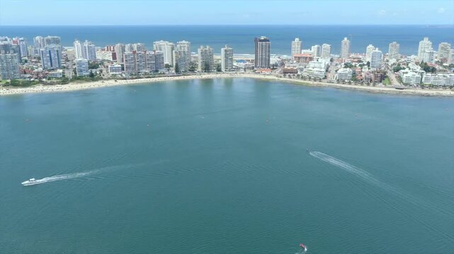 Aerial view of buildings lining the coast with boats speeding through the water, creating a vibrant contrast of urban and marine elements, Punta del Este, Uruguay.