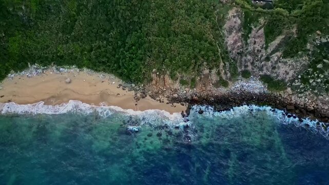 Aerial view of the tranquil beach meeting the lush hillside and the boats in the harbor, a blend of natural beauty and human activity, Keelung, Keelung City, Taiwan.