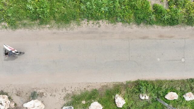 Top-down aerial view of a surfer on a bicycle carrying a surfboard along the Nahariya coastline, Israel