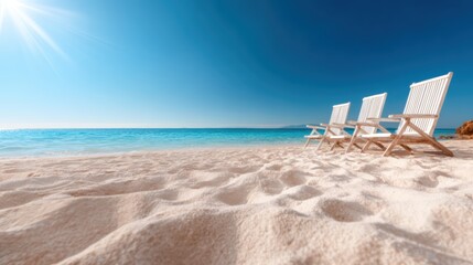 Fototapeta premium Three white chairs sit on a serene sandy beach with calm turquoise waters stretching out under a bright blue sky, evoking peace and relaxation in nature's beauty.
