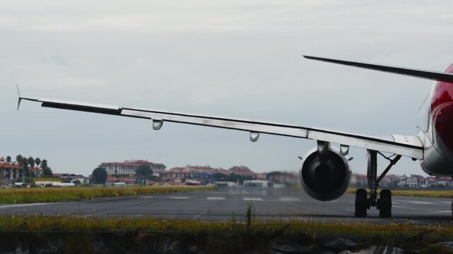Close-up rear view of a passenger jet accelerating for takeoff. The powerful engines kick up a massive cloud of water spray from the wet runway on a rainy, overcast day