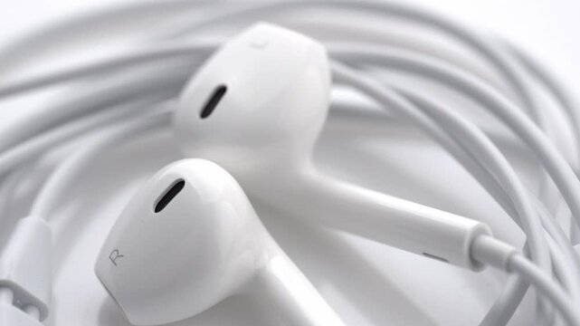 White wired in-ear headphones with USB Type-C connector rotating slowly on a seamless white background. 