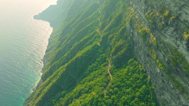 Aerial view of steep green cliffs and a narrow dirt road along the coast at Jabal Shaat on the border between Oman and Yemen.