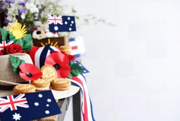Fototapeta premium ANZAC Day military slouch hat with red poppies and biscuits beside Australian flag and rising sun.