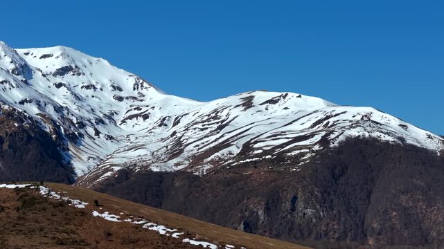 Aerial view of the snowy mountain range under a clear blue sky, creating a stark contrast between the white peaks and brown foothills, Campan, Occitanie, France.