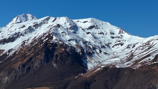 Aerial view of the snow capped mountain peak against the clear sky, a contrast of white and dark earth tones, Campan, Occitanie, France.