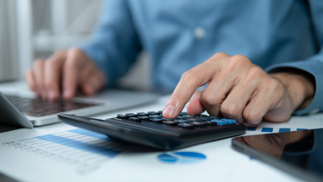 Businessman hands using a calculator to check company finances and earnings and budget.Tax financial plan. Tax income return. Calculating monthly expenses, managing budget, loan documents, invoices.