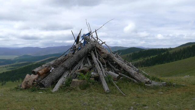Obo (ovoo) is a sacred object in the form of a heap of stones and a hut of logs against the background of low, coniferous forests and picturesque cloudy skies. The Mongolian landscape.