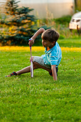 A young boy loses his balance and stumbles after hitting a shuttlecock during a summer badminton game outdoors. Active play, coordination, and fun holiday moments in nature.