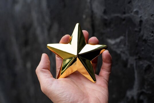 A golden star is being held in a hand against a textured gray background.