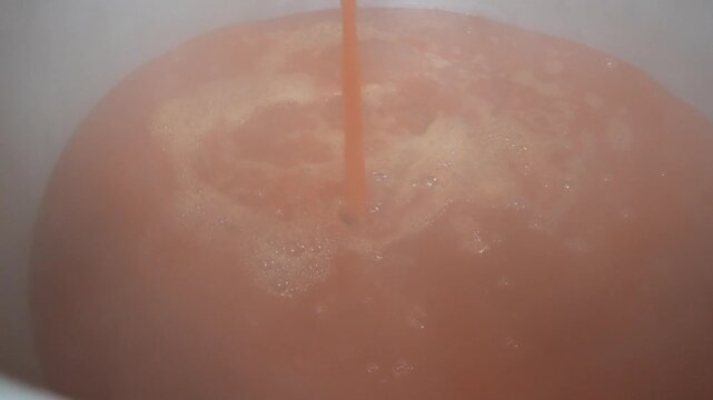 Ladle pouring red broth into large pot