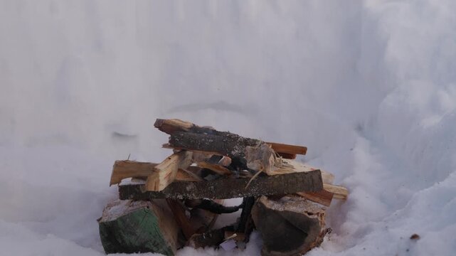 Small campfire burning inside a deep snow pit during winter. Firewood slowly burns while smoke rises into the cold air surrounded by high snow walls. High quality 4k footage