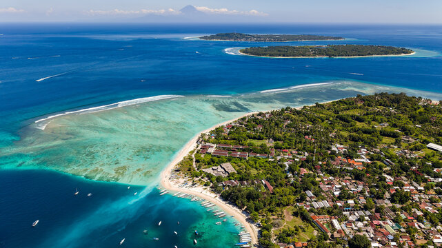 High angle view over lush coastal village, blue ocean, boats and distant mountain peaks