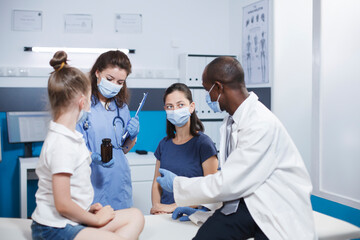 Obraz premium Multiracial healthcare workers recommend a bottle of pills as recovery treatment to mother of a small child in cabinet. Physician giving flask with prescription medicine to a woman with a little girl.