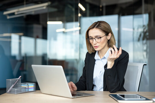 Businesswoman thinking critically while working on a laptop, facing a complex problem or project in a modern office environment, contemplating solutions with a focused and frustrated expression
