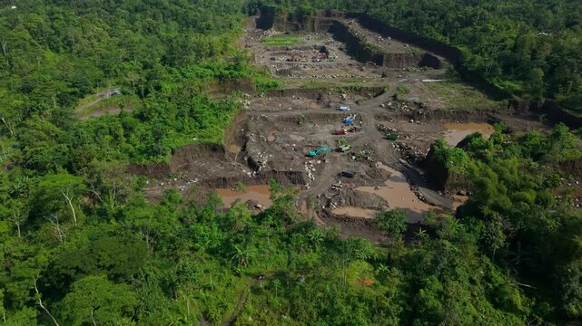 Aerial view of a large deforestation area with heavy machinery contrasts against the dense green forest and a merapi mountain backdrop, Kali woro, Klaten, Indonesia.