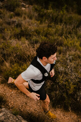 Fototapeta premium High angle view of a trail runner running along a narrow dirt path through rugged mountain terrain. Outdoor adventure fitness and endurance sport in natural wilderness